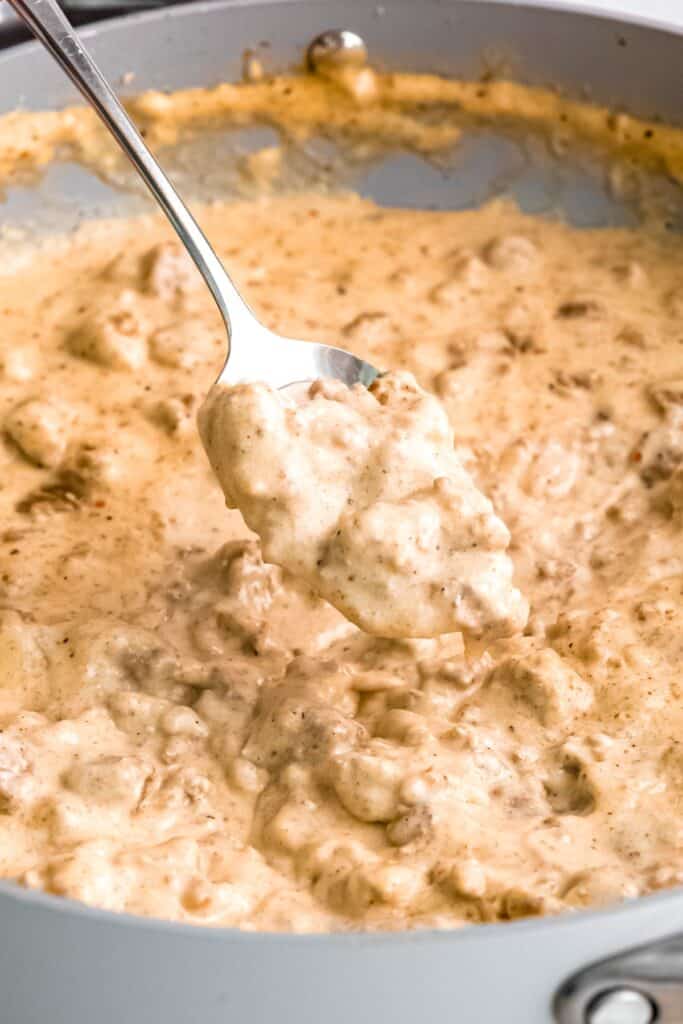 closeup 45 degree angle shot of a silver spoon taking a spoonful of classic sausage gravy from the skillet, showing the thick consistency.