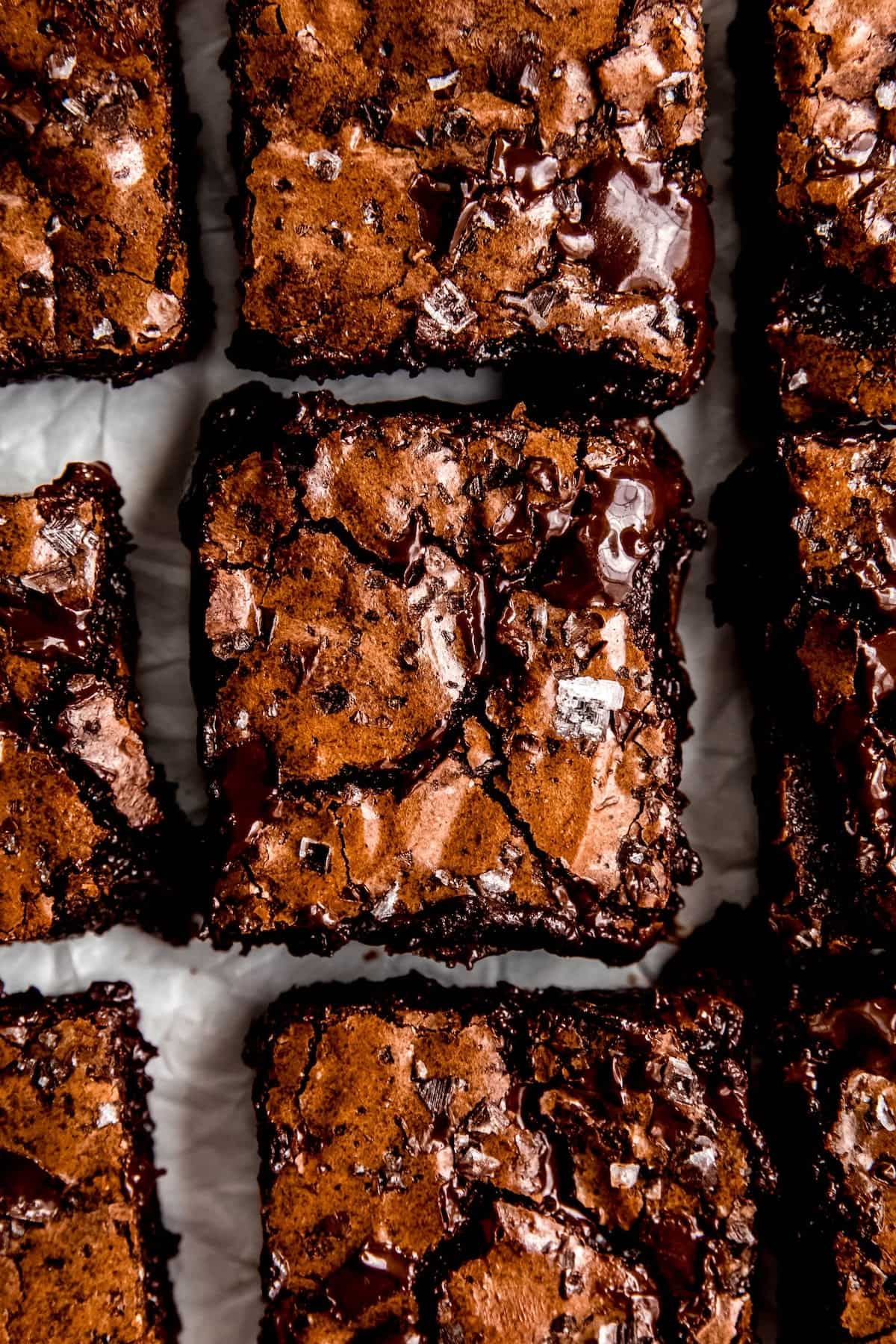 closeup overhead shot of double dark chocolate brownies after slicing; you can see flakes of maldon sea salt and pools of melty chocolate interrupting the shiny, crisp topping.