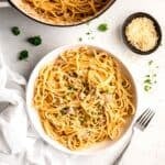 overhead shot of a white table with a pot of easy canned clam linguine with a white pasta bowl filled with a portion of it topped with fresh parsley and cheese.