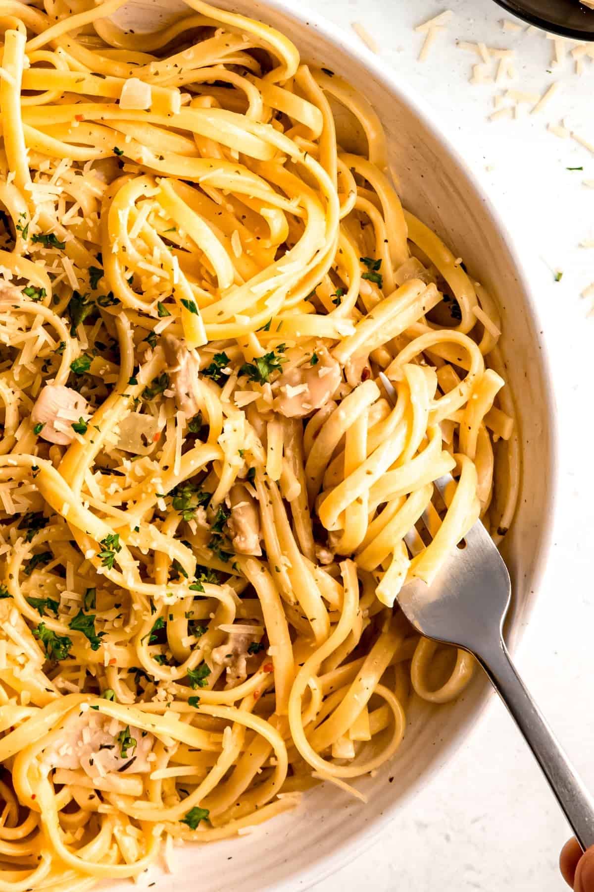 closeup overhead shot of a silver fork with a twirl of easy linguine and clams in a white pasta bowl.