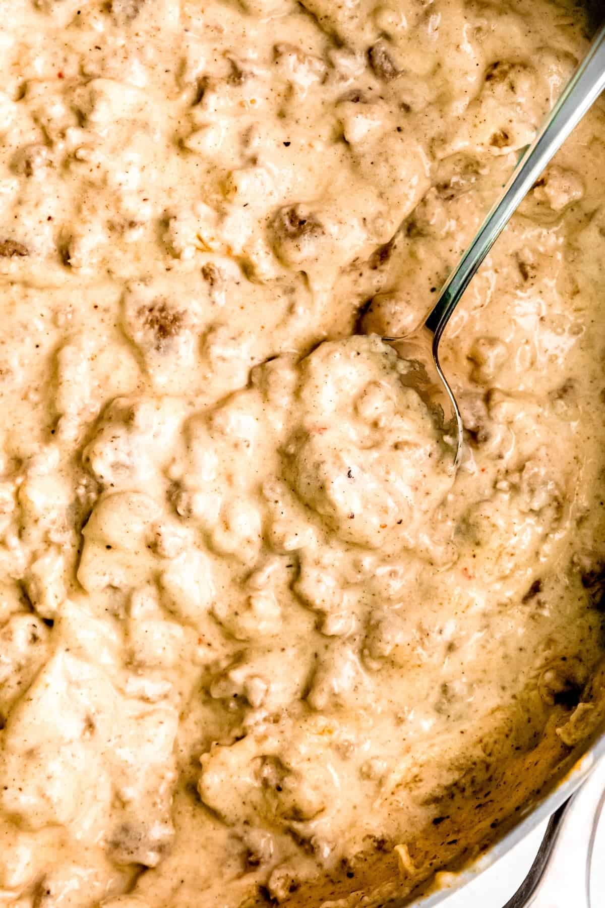 closeup overhead shot of a silver spoon taking a bite of country sausage gravy from the skillet.