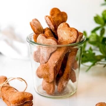 square hero image of a clear jar filled with homemade banana peanut butter dog treats shaped like bones.