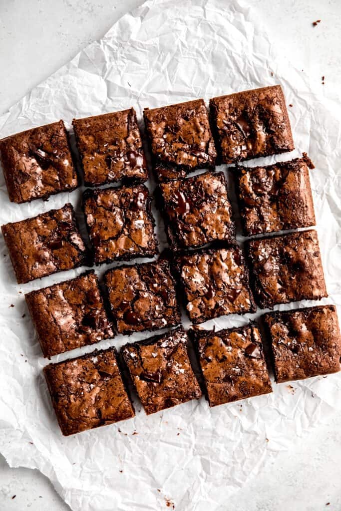 flat lay shot of dark chocolate brownies on a piece of crumpled white parchment paper after slicing into 12 squares.