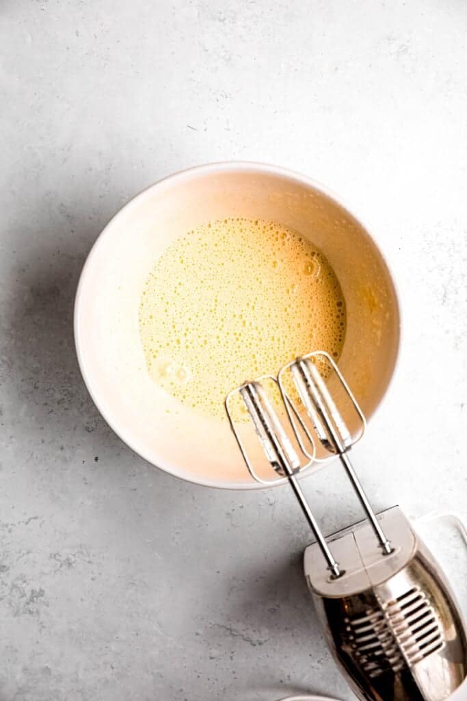 remaining egg and sugar mixture getting beaten in a bowl until pale yellow and fluffy with a ribbony texture.