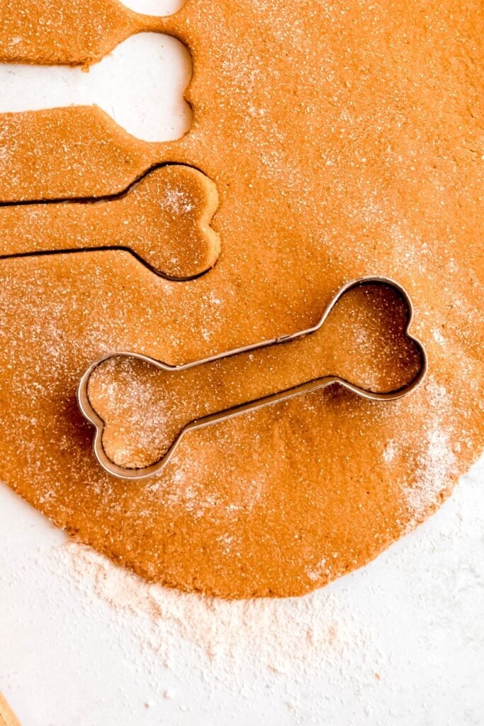 closeup shot of a a bone-shaped cookie cutter cutting out pieces of homemade dog treat dough.