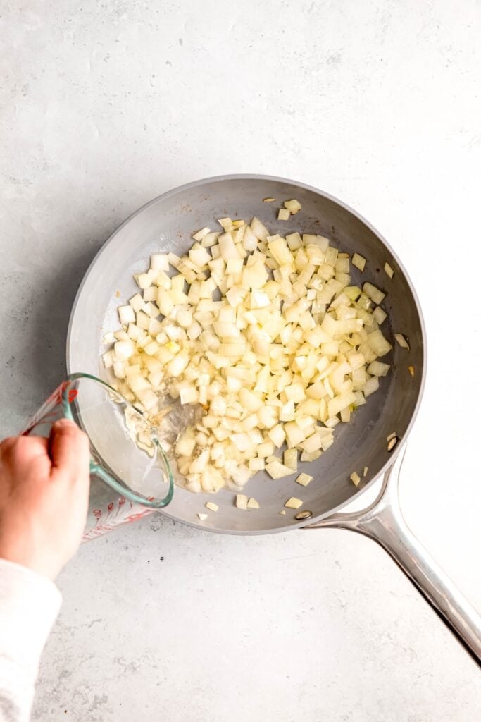 action shot of white wine being poured into the skillet with the sautéed onions.
