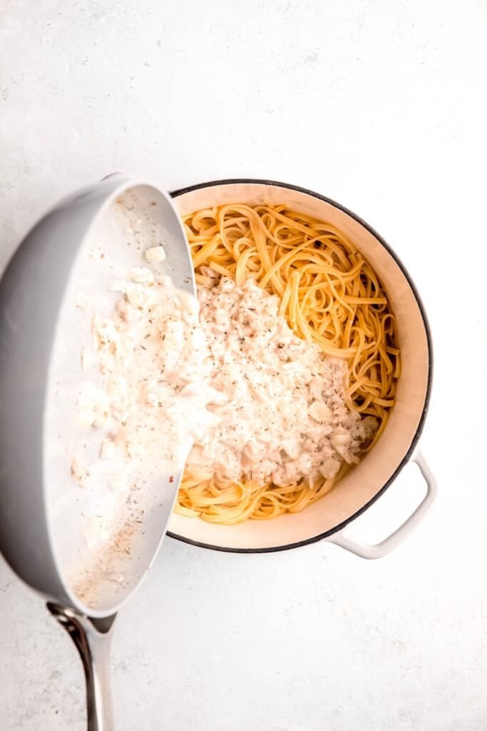 action shot of creamy white wine clam sauce being poured into the dutch oven with the drained linguine.