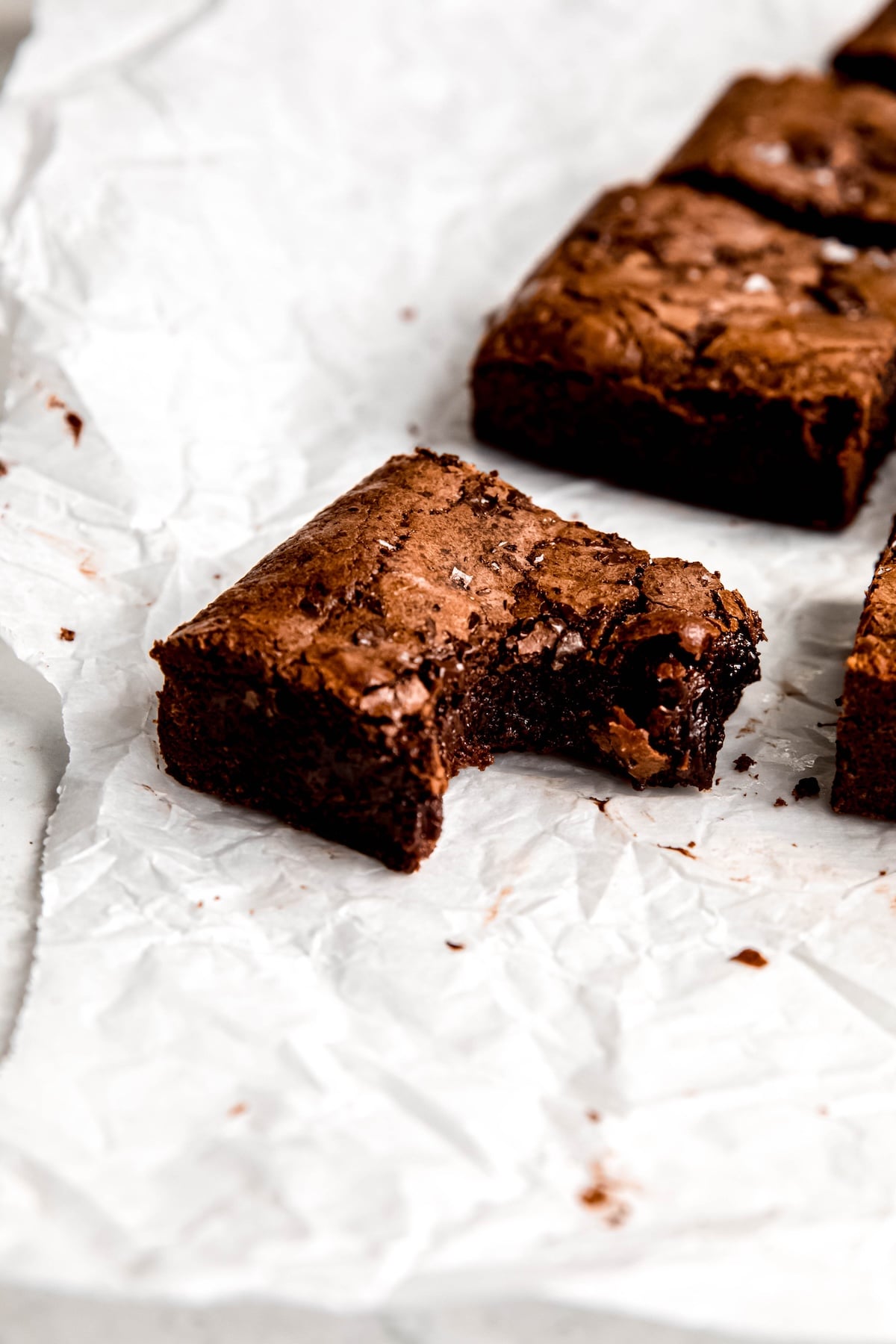 closeup shot of a single corner piece of julia child's fudgy brownies on a crumpled piece of parchment paper showing the fudgy interior; the rest of the sliced brownies are faded in the background.