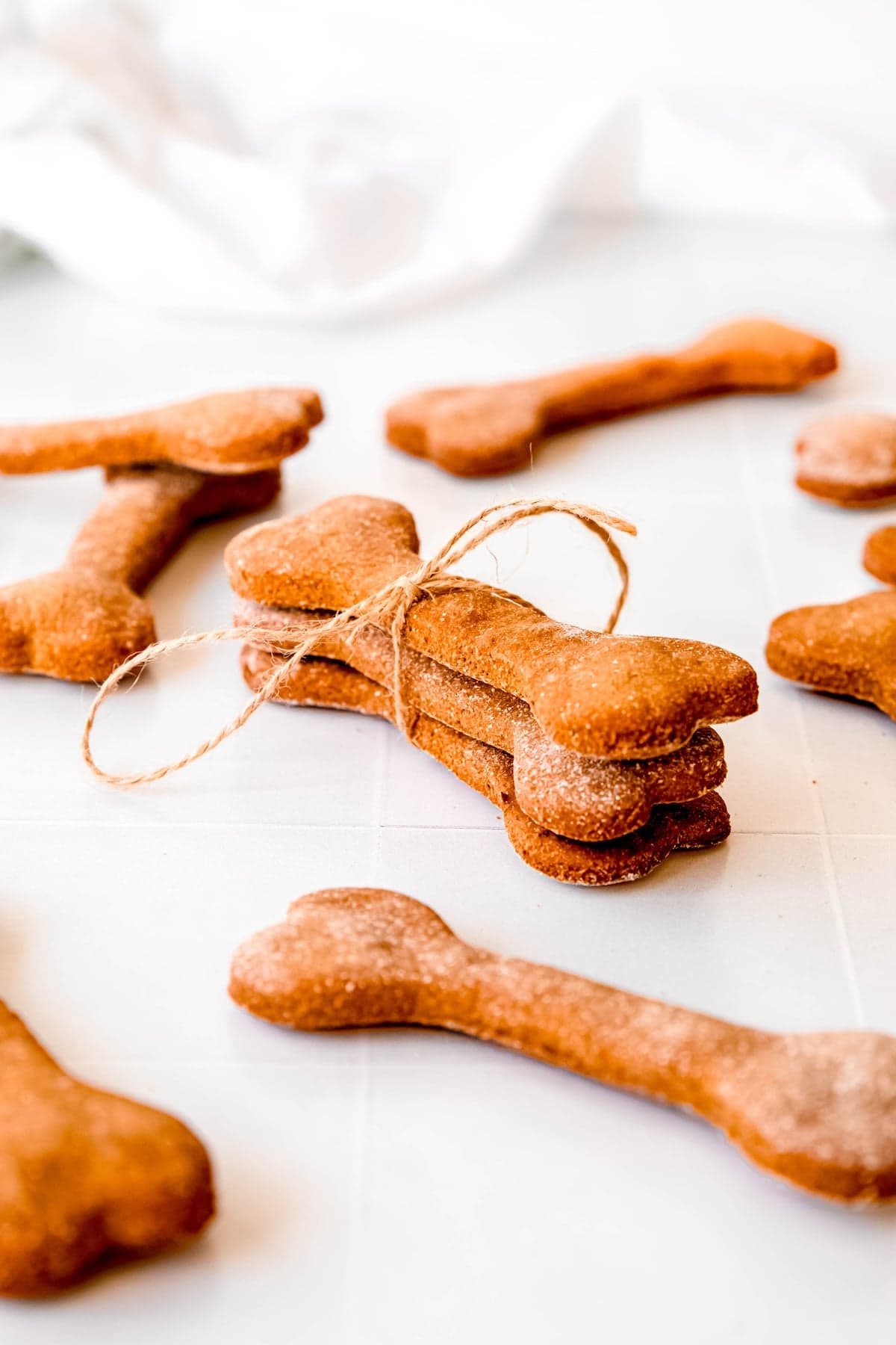 stack of 3 oat peanut butter banana dog treats tied with twine with more scattered around them on a white table.