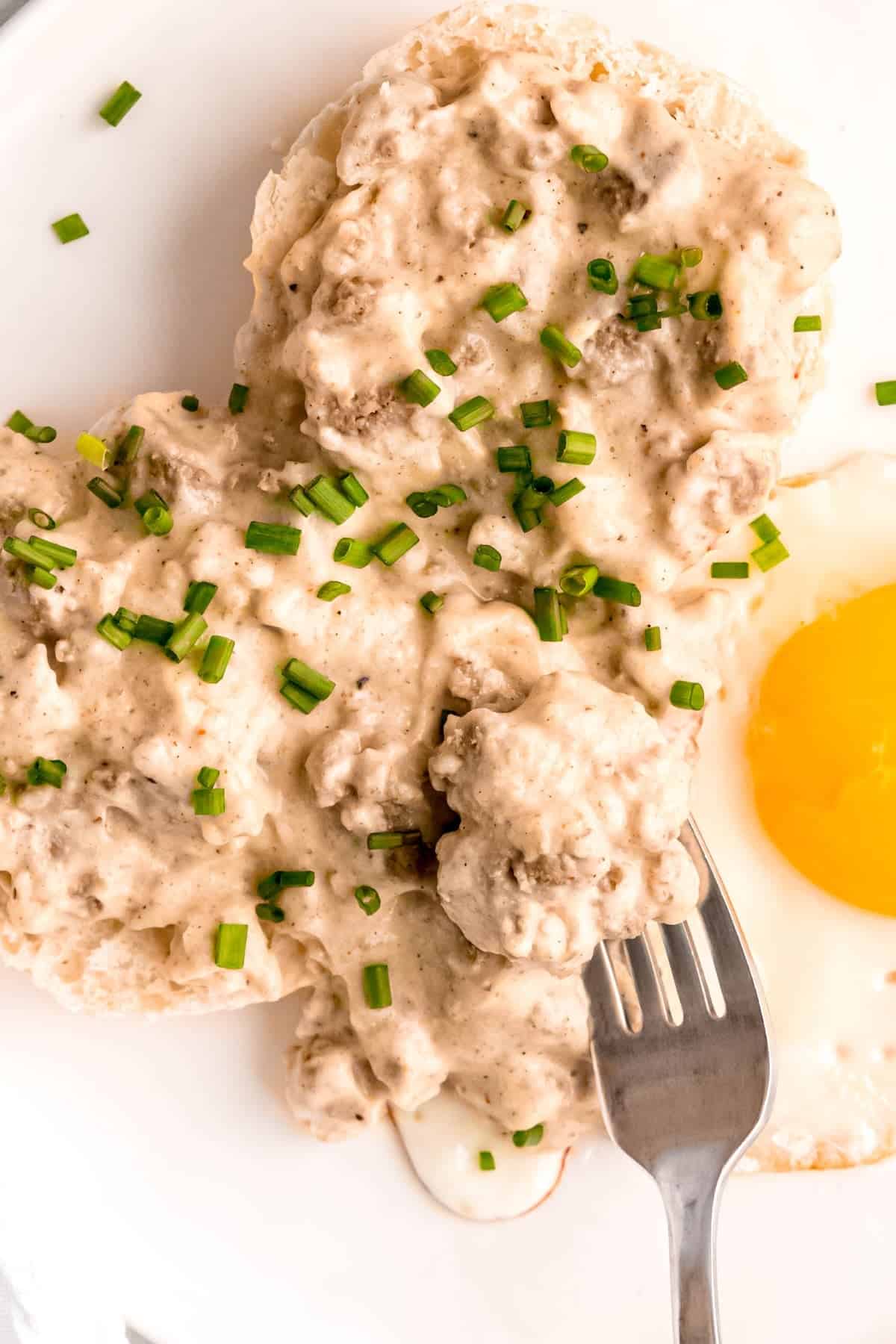 closeup overhead shot of old fashioned biscuits and gravy with a fried egg; a silver fork is taking a bite.