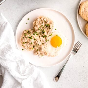 square hero image of a plated portion of old fashioned southern sausage gravy on a biscuit with a fried egg for breakfast.