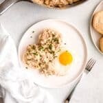 overhead shot of sausage gravy and biscuits plated up with a sunny side up egg and fresh chives on a white plate with a silver fork.