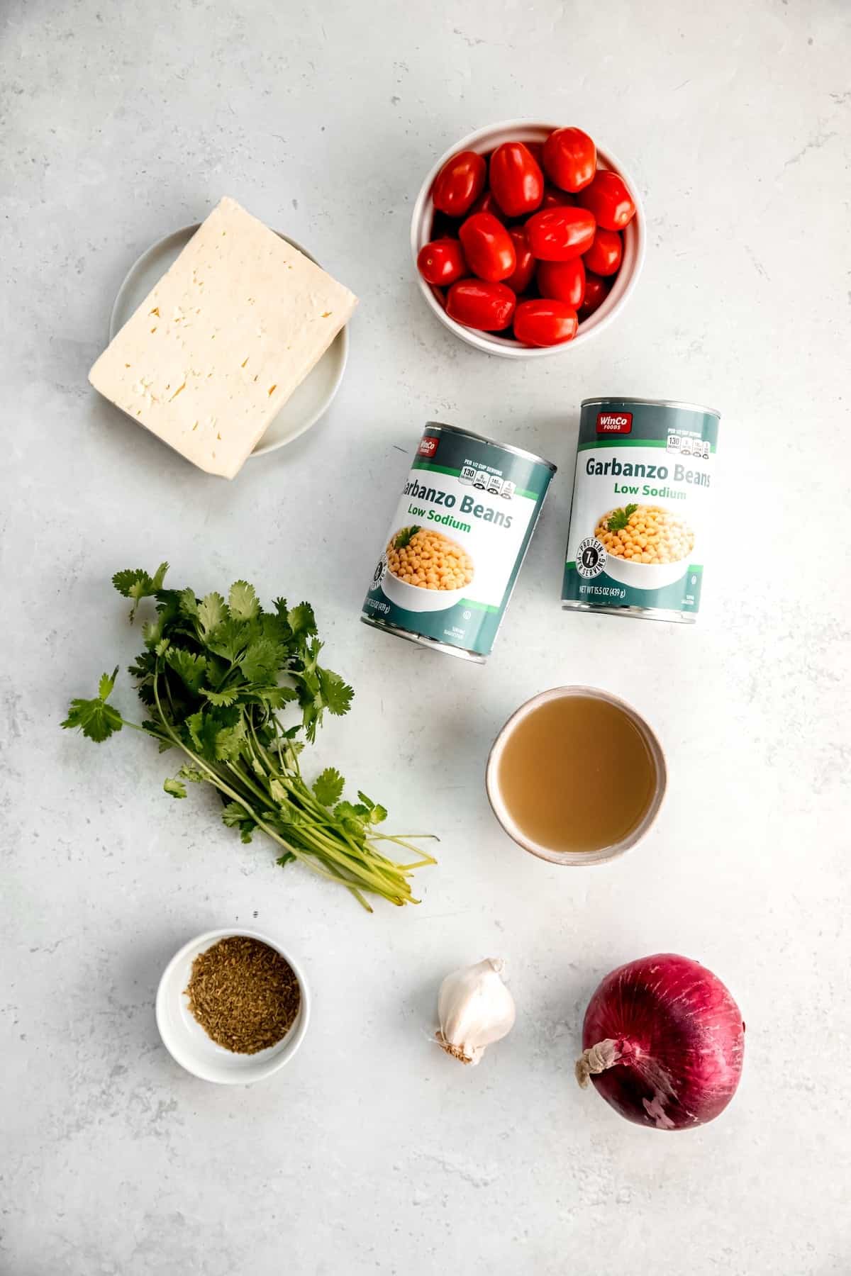 ingredients needed to make Mediterranean baked feta with tomatoes and chickpeas measured out on a white table.