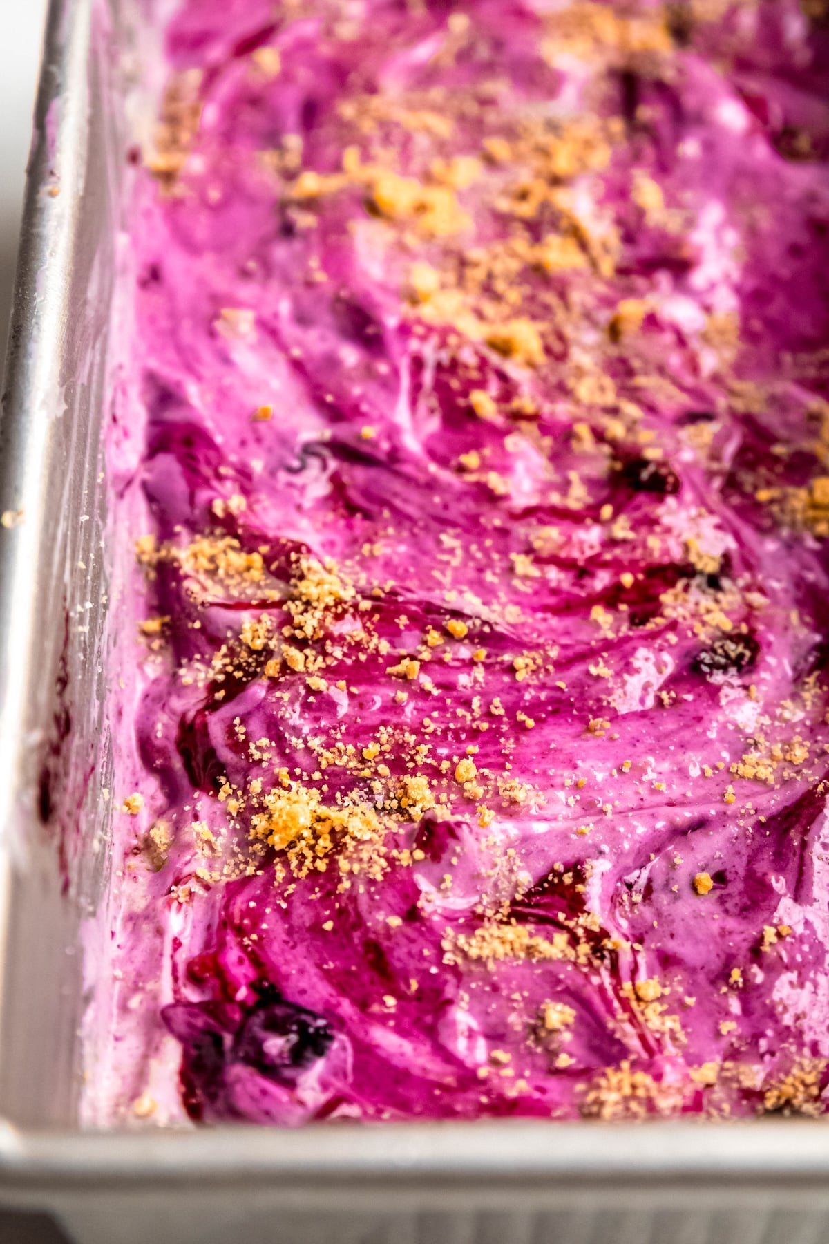 closeup shot of blueberry ice cream with a graham cracker swirl freezing in a loaf tin.