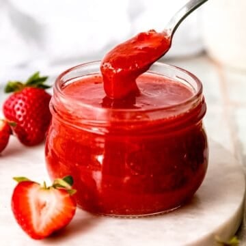 square hero shot of canned strawberry jam with pectin with a spoon taking a bite showing the viscosity.