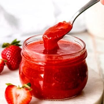 hand taking a silver spoonful of canned strawberry jam from a half pint jar showing the thick viscosity of the jam thanks to the pectin.