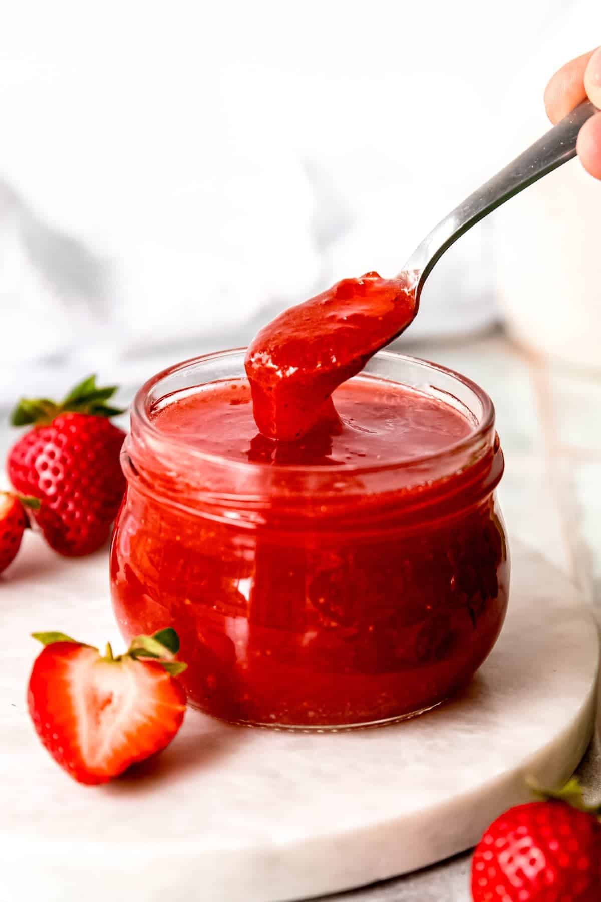 hand taking a silver spoonful of canned strawberry jam from a half pint jar showing the thick viscosity of the jam thanks to the pectin.