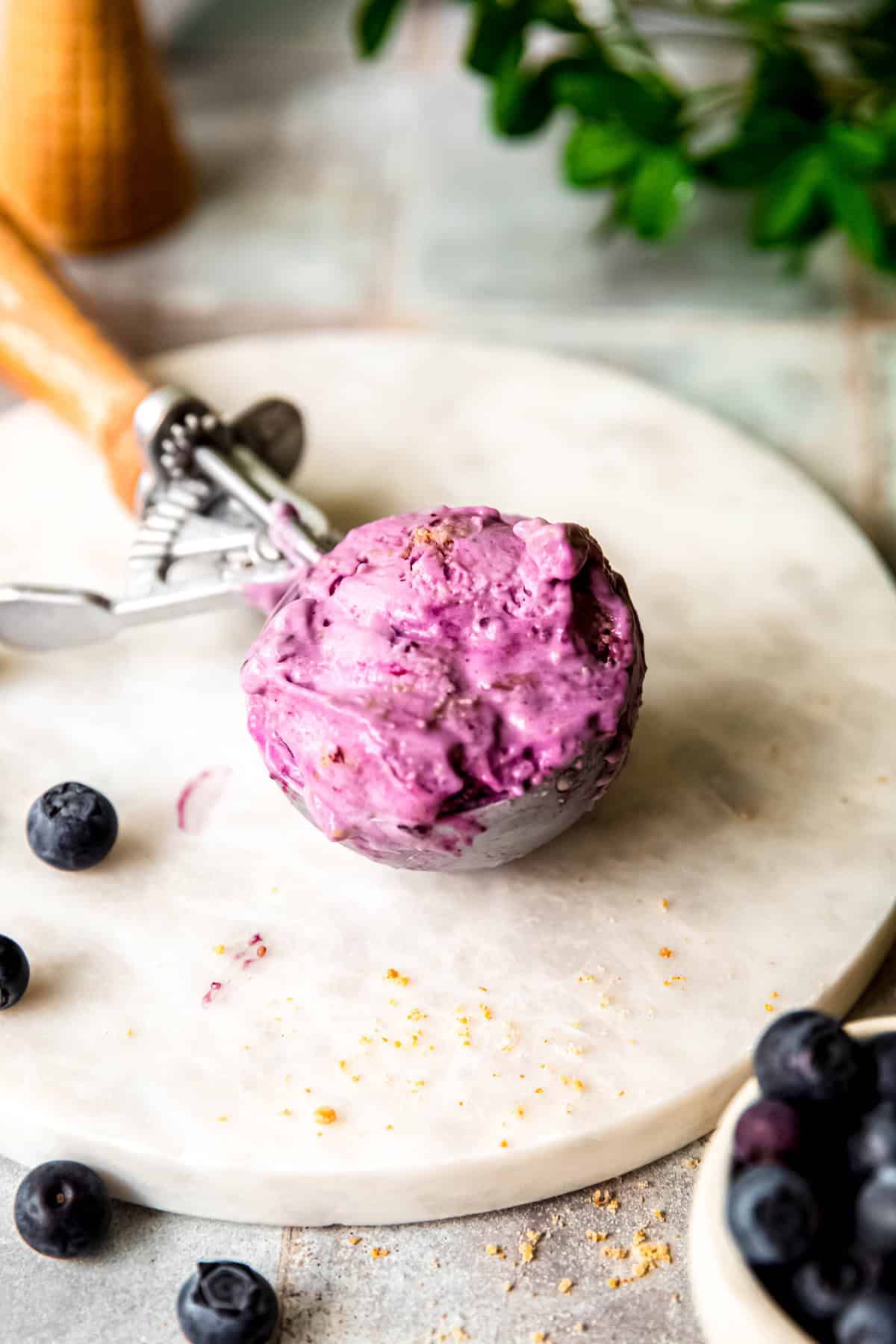 spring loaded wooden handled ice cream scoop with a scoop of fresh blueberry ice cream with graham cracker crumbles.