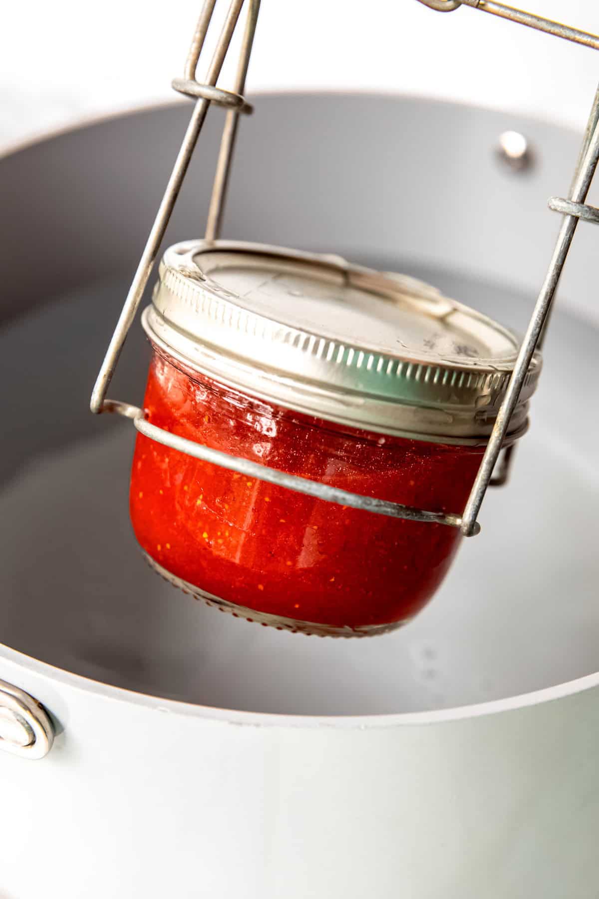 can lifter removing a processed jar of canned strawberry jam from a water bath canner.