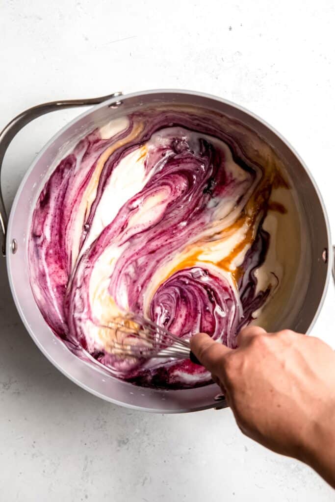 hand whisking blueberry sauce and vanilla into the thickened cheesecake ice cream base.