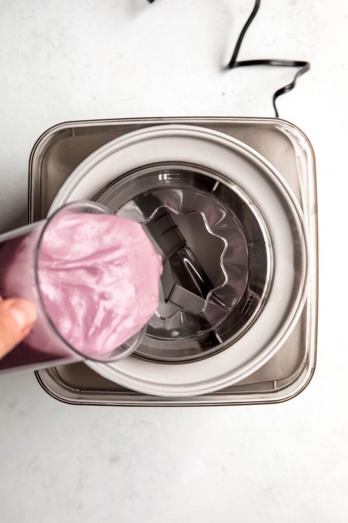 hand pouring blueberry ice cream base into an ice cream maker to churn.