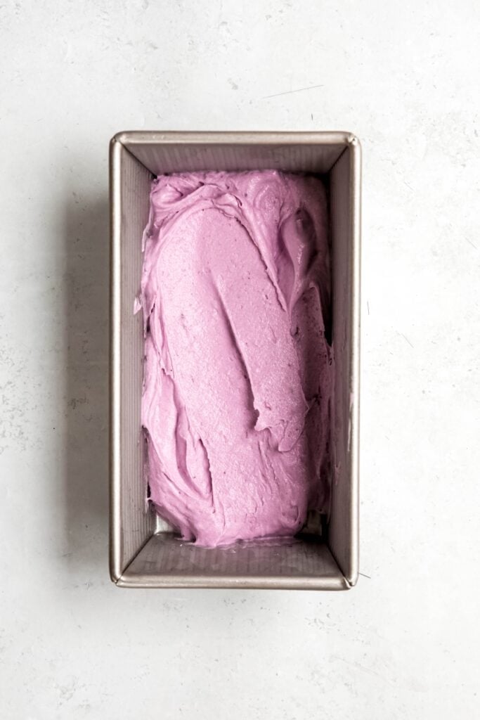 blueberry ice cream packed into the base of a silver loaf tin before adding the layers of graham cracker crumbles and blueberry sauce.