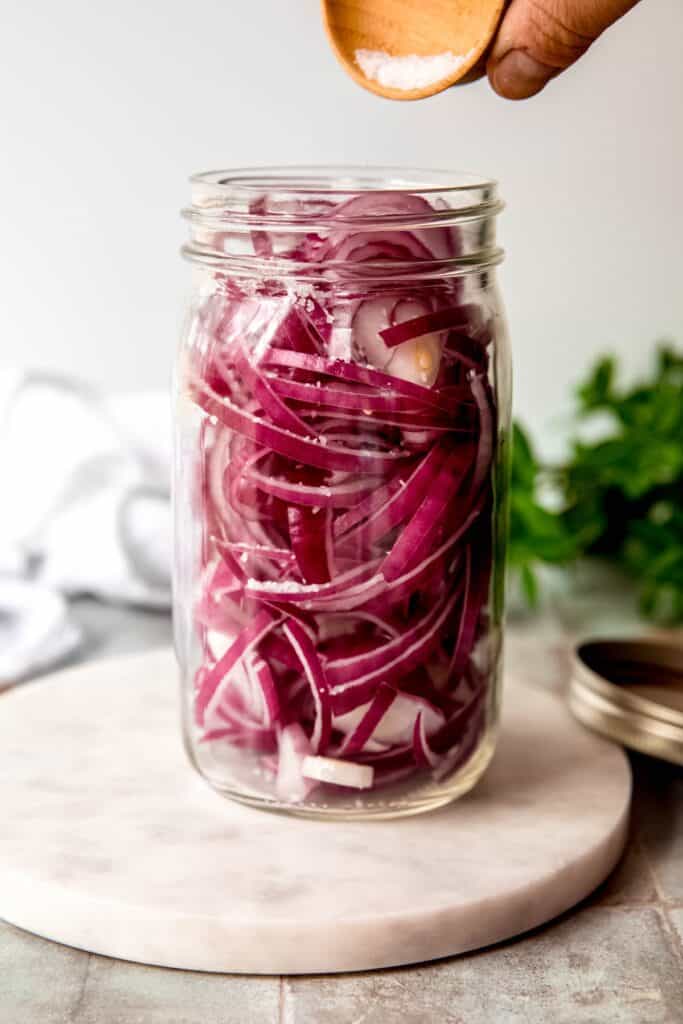 action shot of salt being sprinkled over the onion slices in the jar.