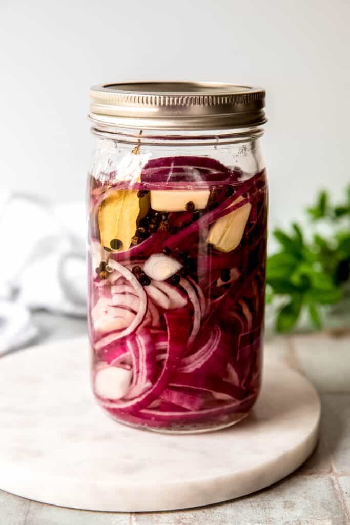 jar of thinly sliced onions with garlic cloves, bay leaves, peppercorns, allspice berries, and rice vinegar marinating to become pickled onions.