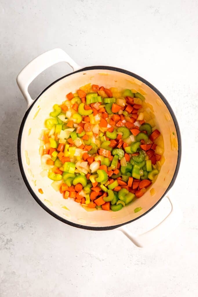 carrots, onions, and celery being sautéed in a white dutch oven.