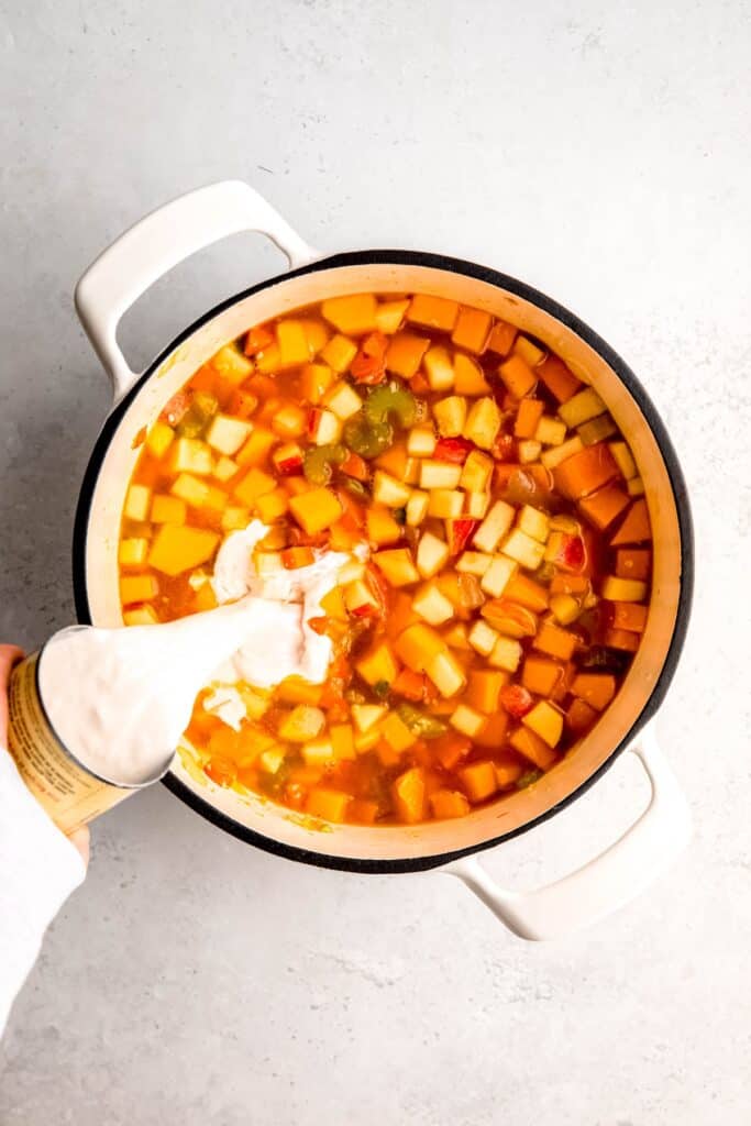 action shot of coconut milk being poured into the dutch oven with the broth and veggies.