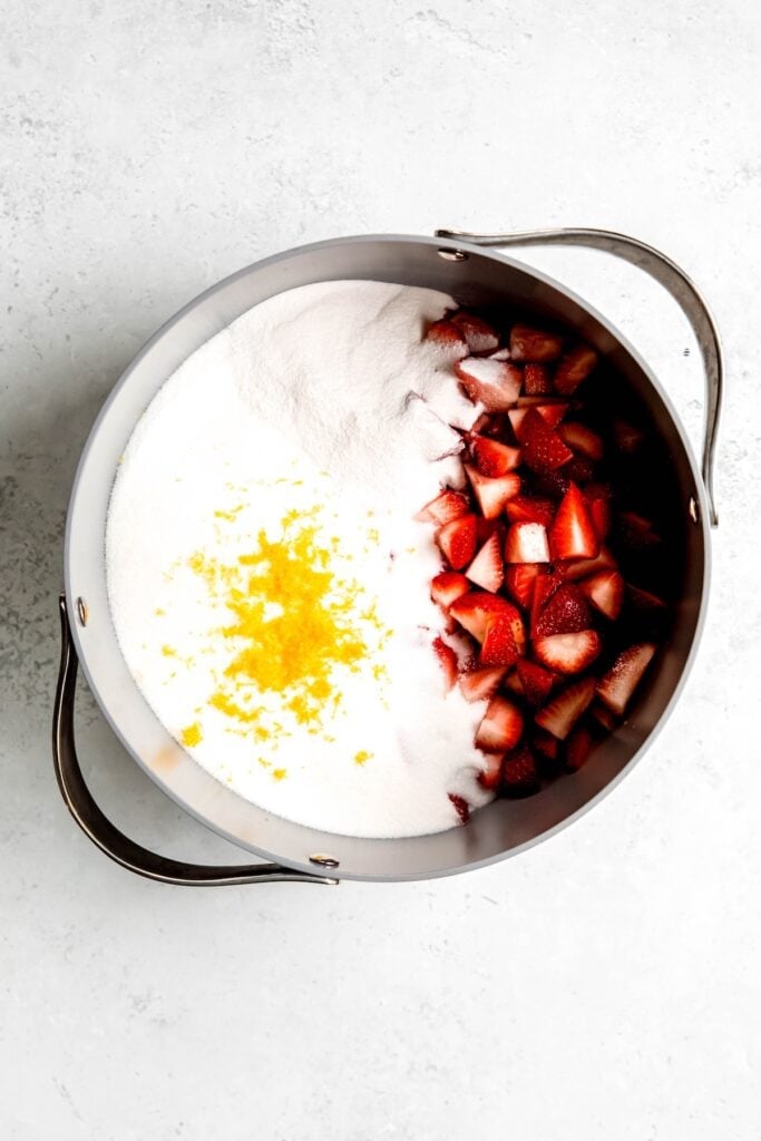 sugar, pectin, lemon juice, lemon zest, and chopped strawberries added to a large pot.