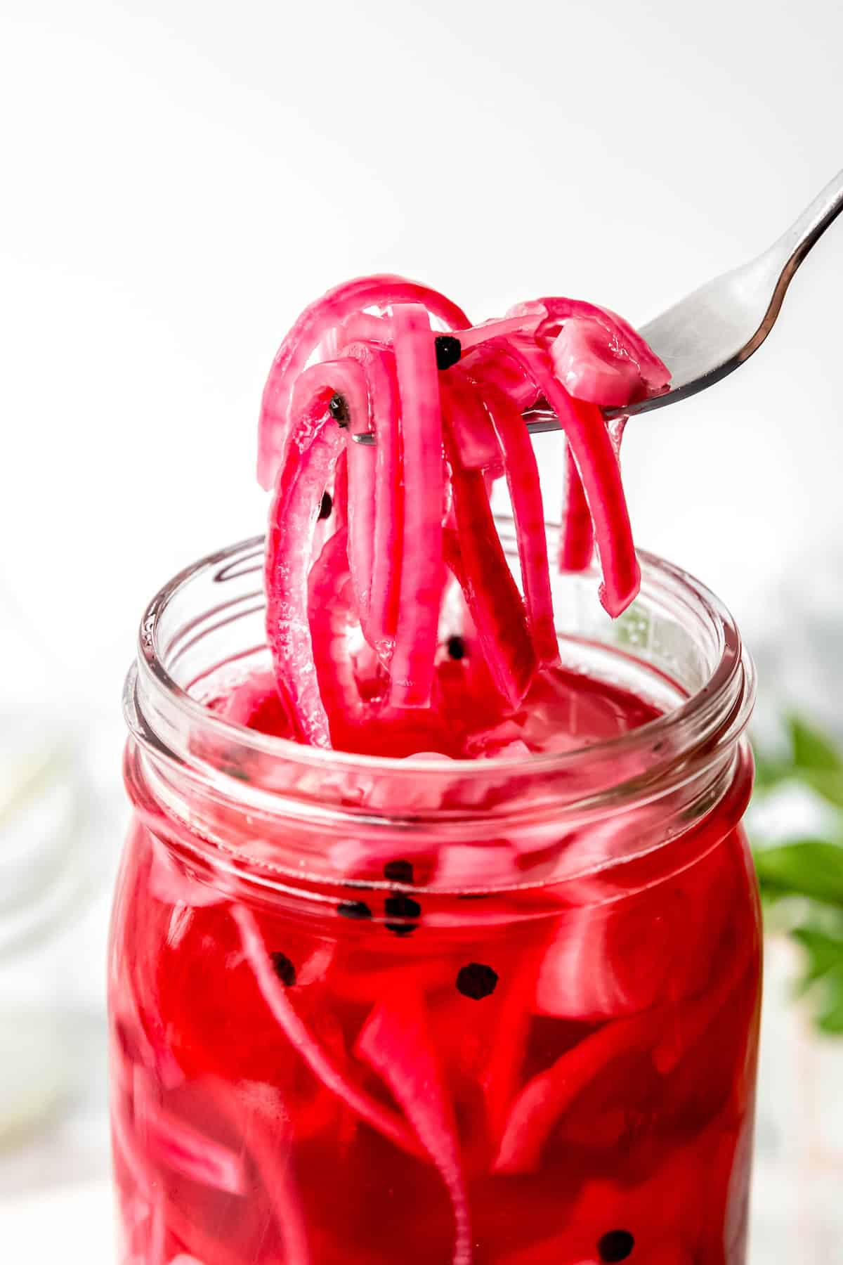 closeup on a forkful of vibrant pink quick pickled onions on a silver fork.