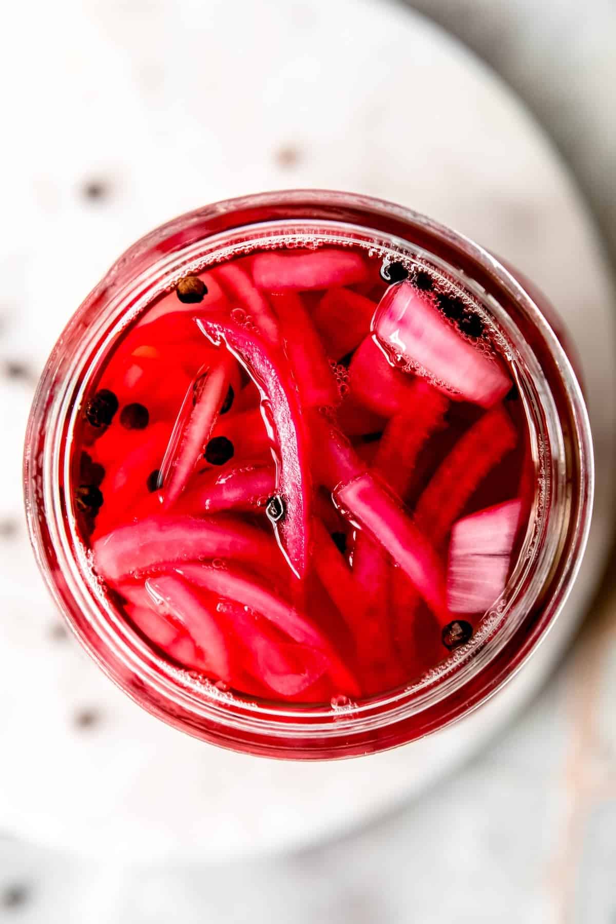 flat lay shot of quick pickled red onions in a jar on a white table.