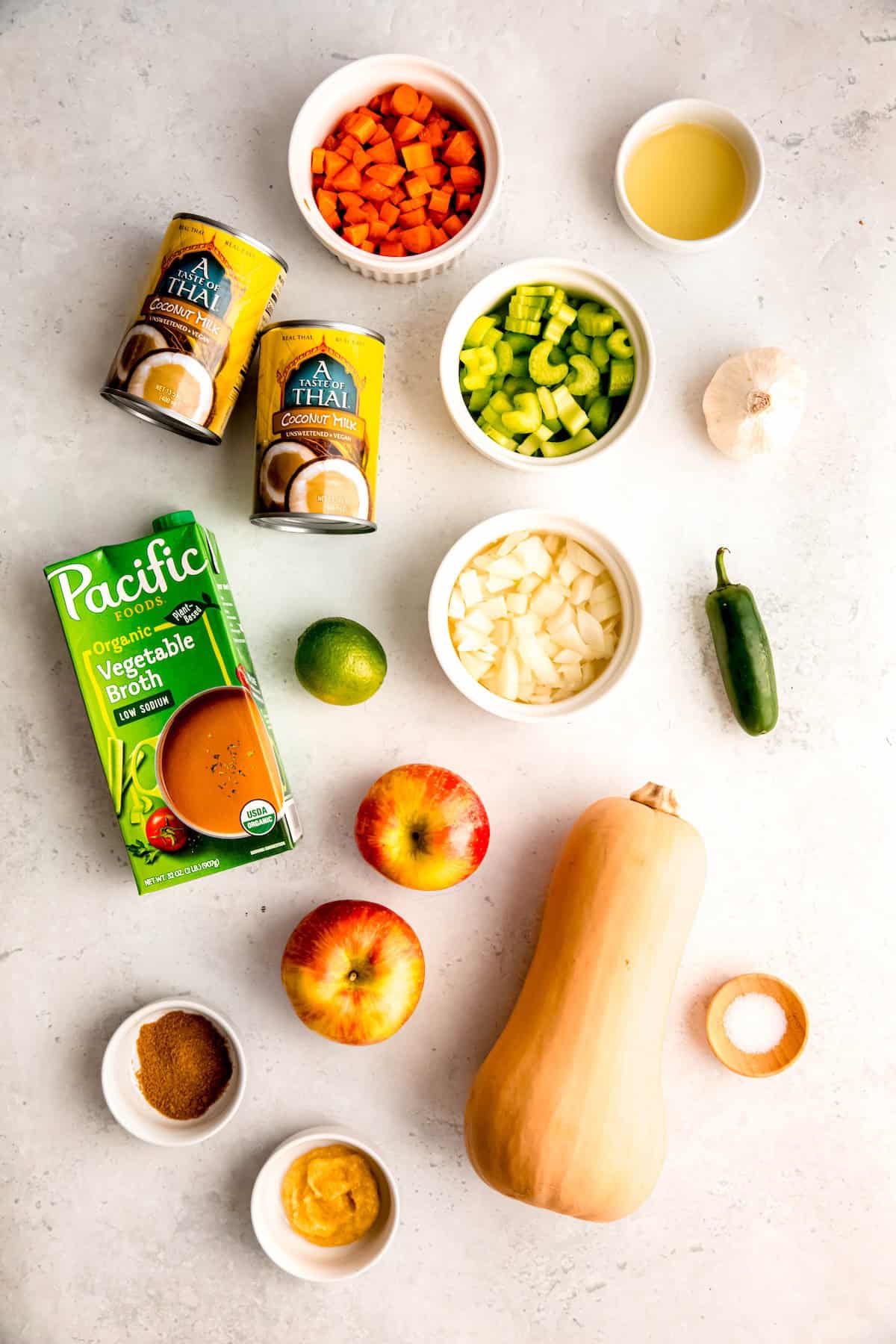 ingredients needed to make spicy butternut squash soup with apples measured out on a white table.
