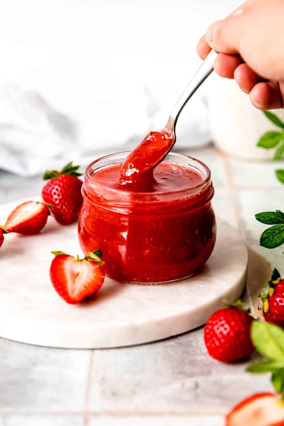 hand dipping a silver spoon into a jar of canned strawberry jam with Sure Jell pectin.