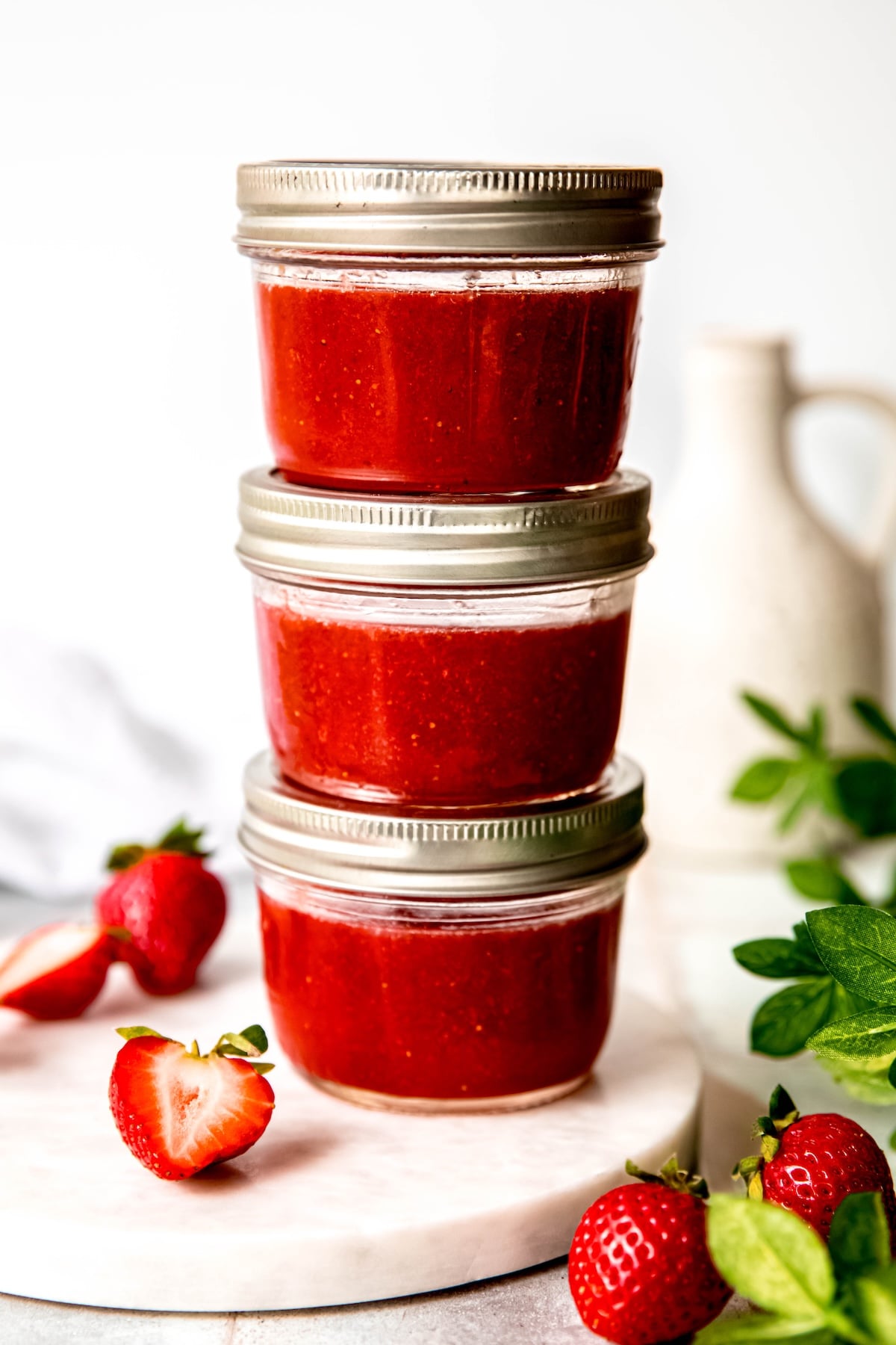3 half pint jars filled with Sure Jell strawberry jam stacked on each other on a white table with fresh strawberries.