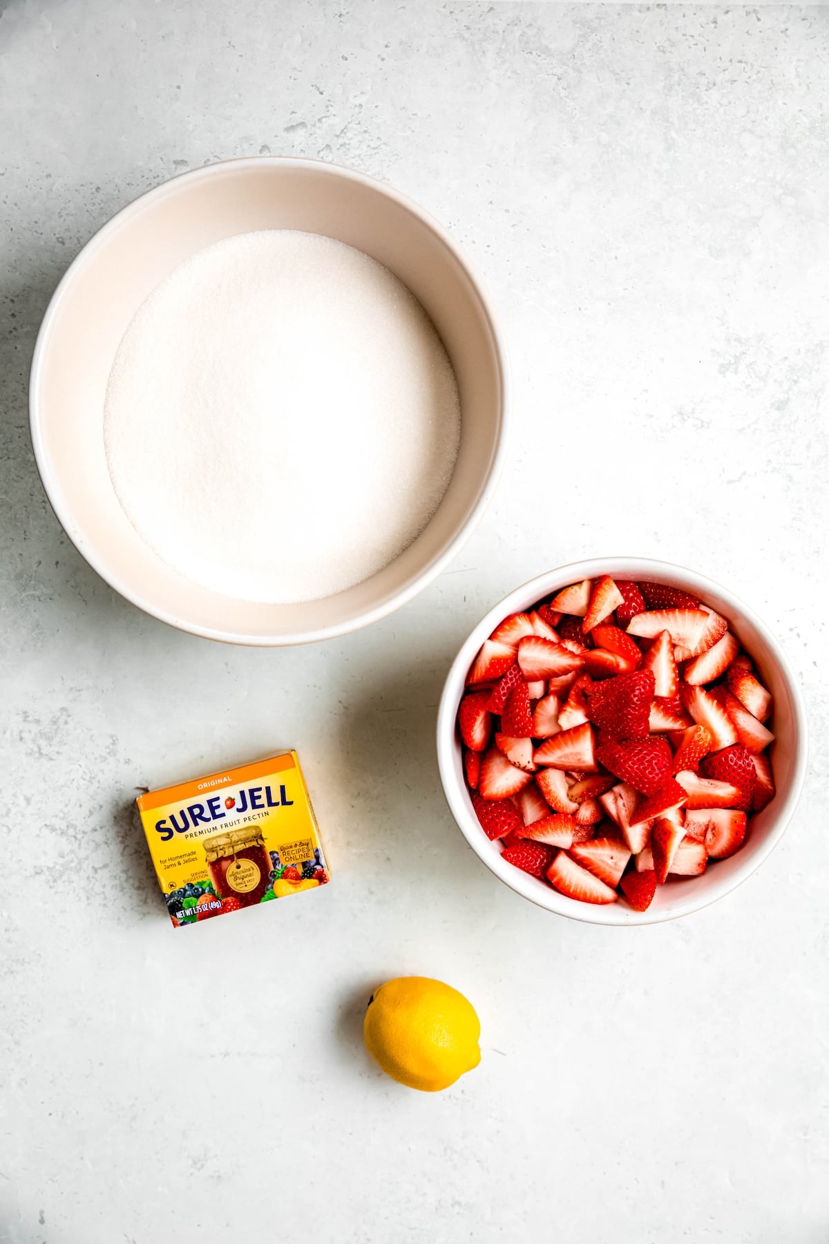 lemon, sure jell pectin, sugar, and chopped strawberries measured out for making homemade strawberry jam for canning.