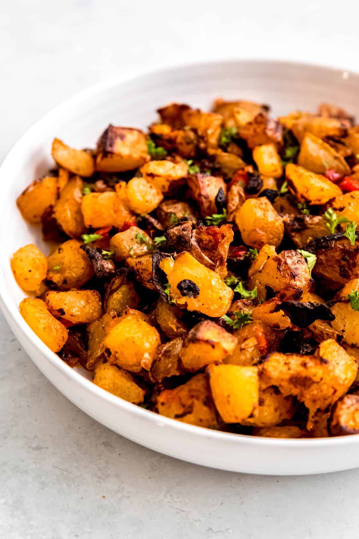 45 degree angle closeup shot of a serving platter of baked home fries sprinkled with fresh parsley.
