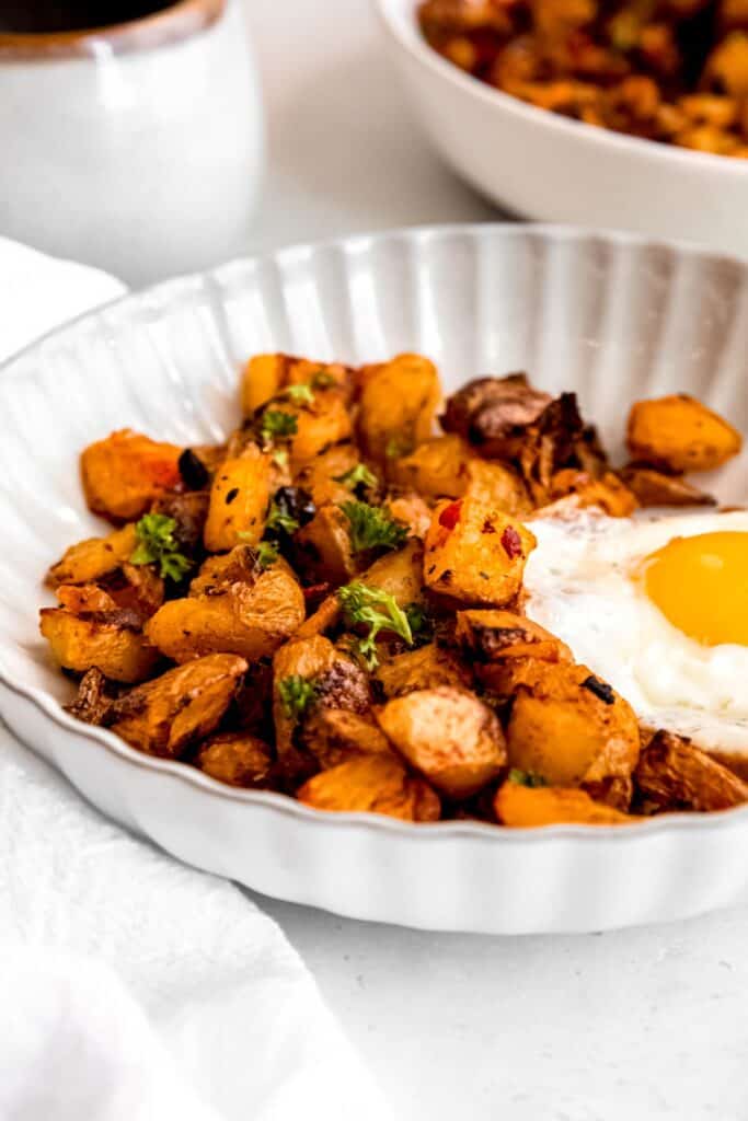 45 degree angle closeup shot of baked home fries in a bowl topped with parsley; you can see the charred edges and colorful peppers.