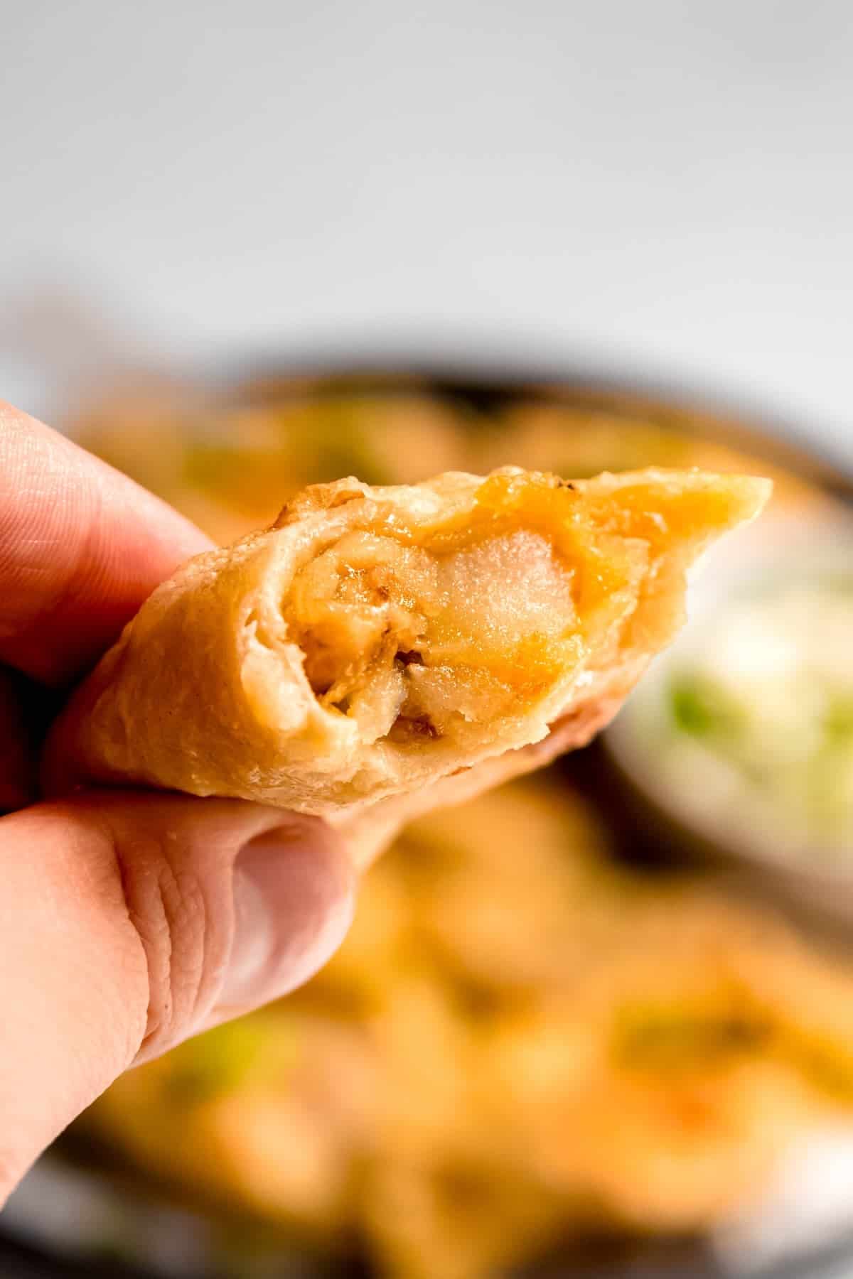 hand holding a pierogi with a bite taken out showing the potato and cheese filling.