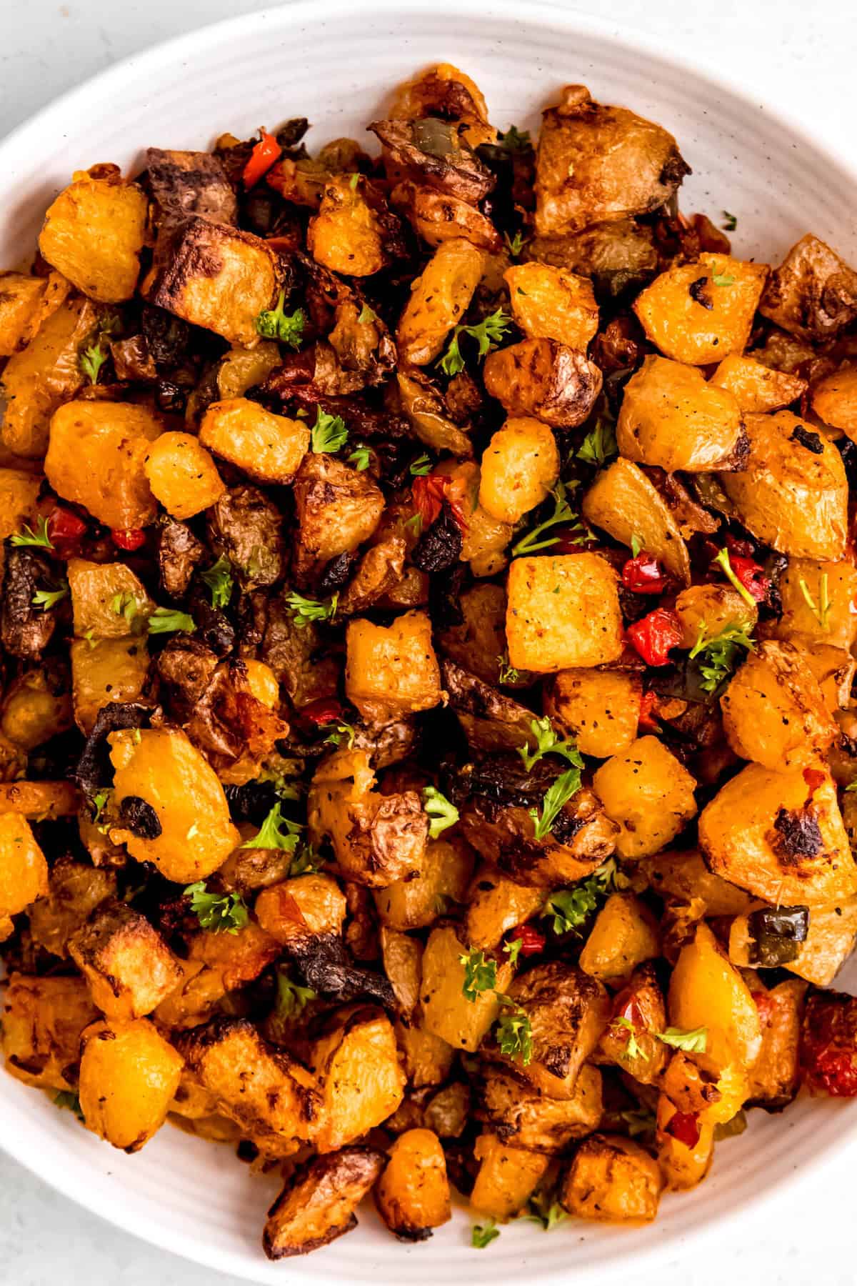 Round white serving bowl filled with crispy baked home fries with peppers and onions.