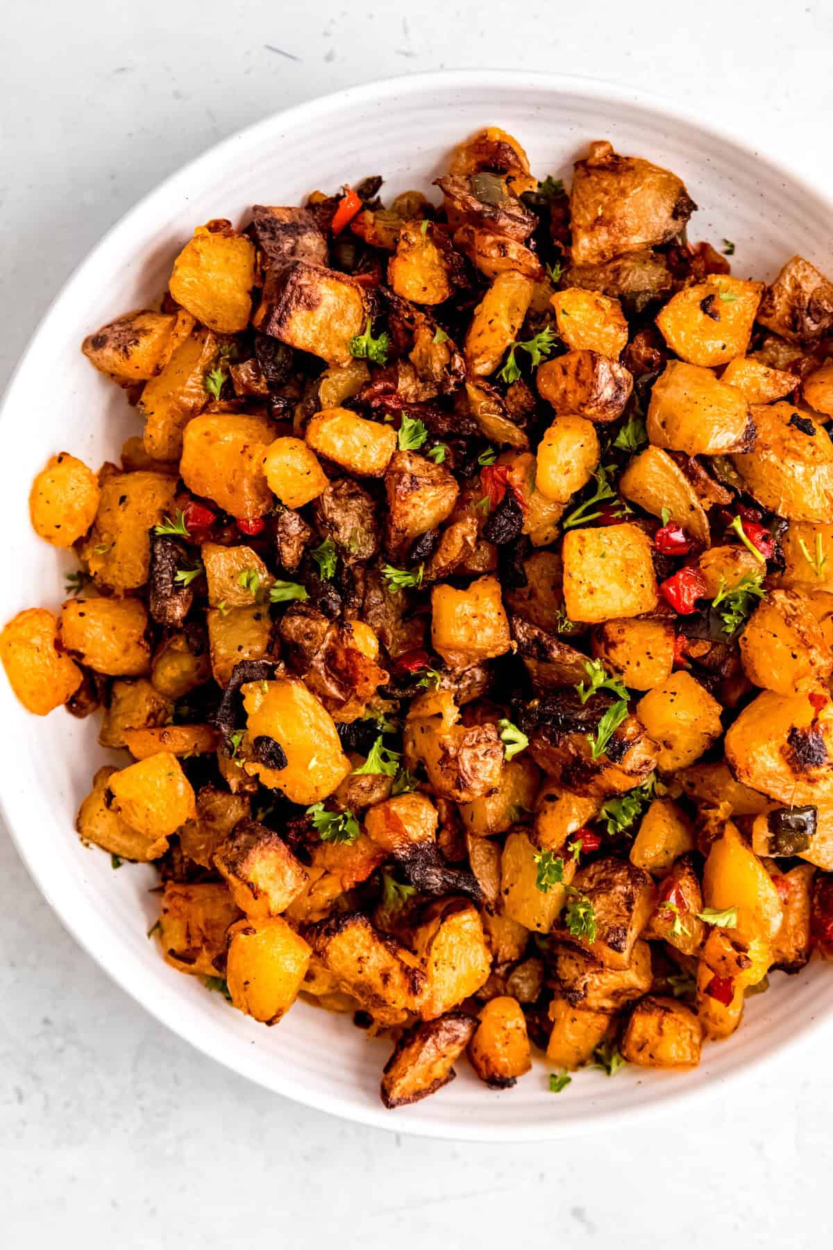 closeup overhead shot of a serving bowl of freshly made homemade home fries topped with parsley.