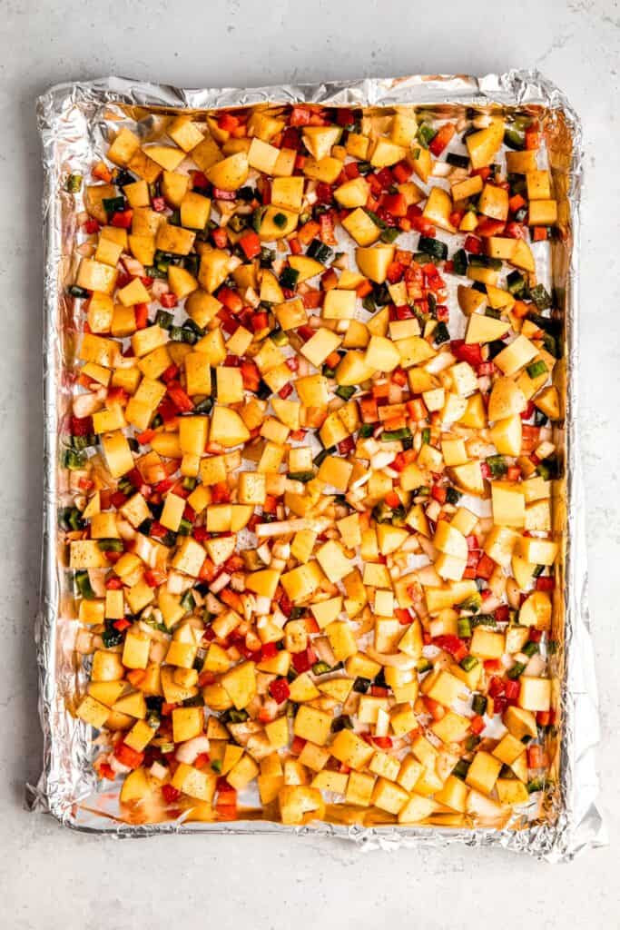 potatoes, onions, peppers, oil, and seasoning all tossed together and spread out on a foil lined sheet pan.