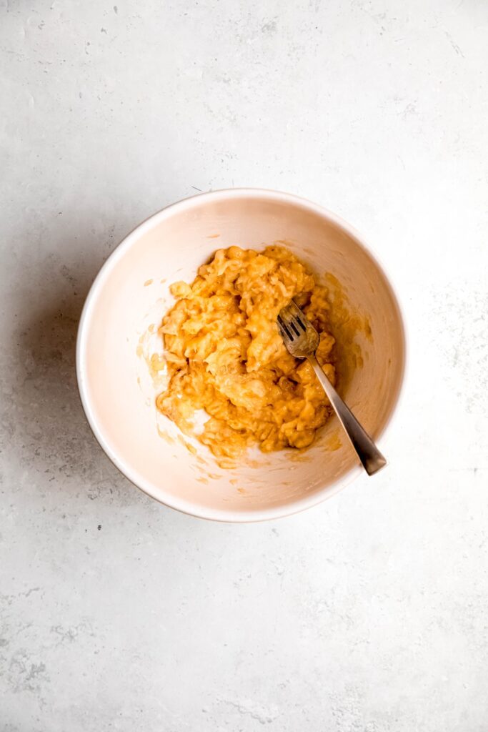 mashed bananas in a mixing bowl with a silver fork.
