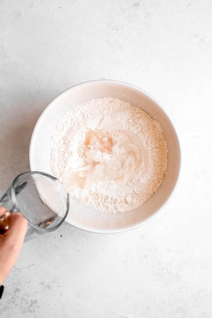 action shot of water being added to the bowl with the flour, salt and egg for making pierogi dough.