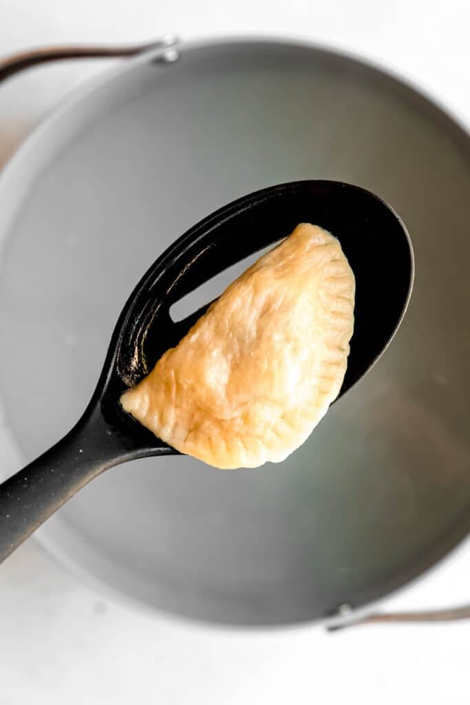 slotted spoon removing a boiled pierogi from the salted water.
