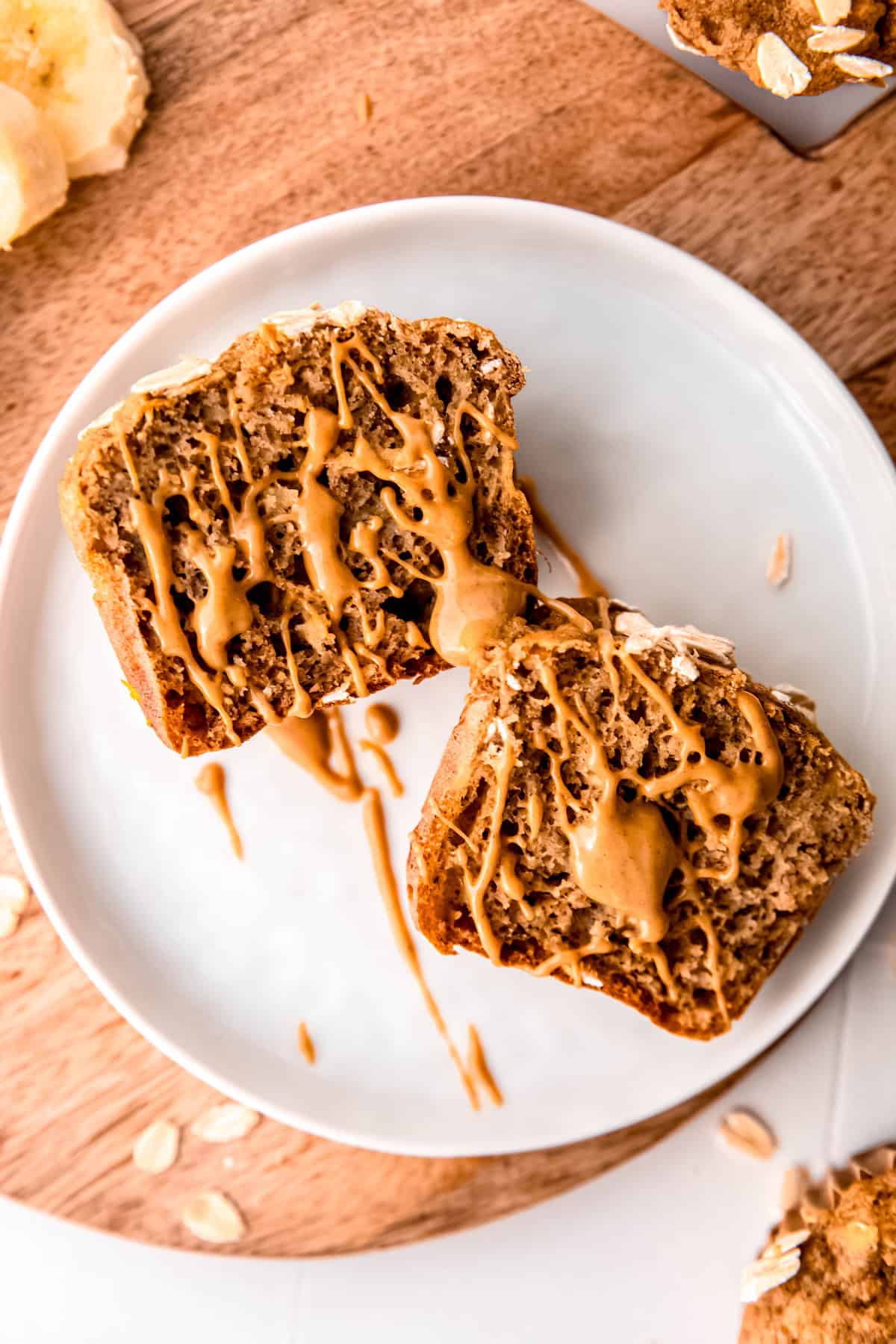 overhead shot of a halved healthy whole wheat banana muffin drizzled with nut butter on a white table.