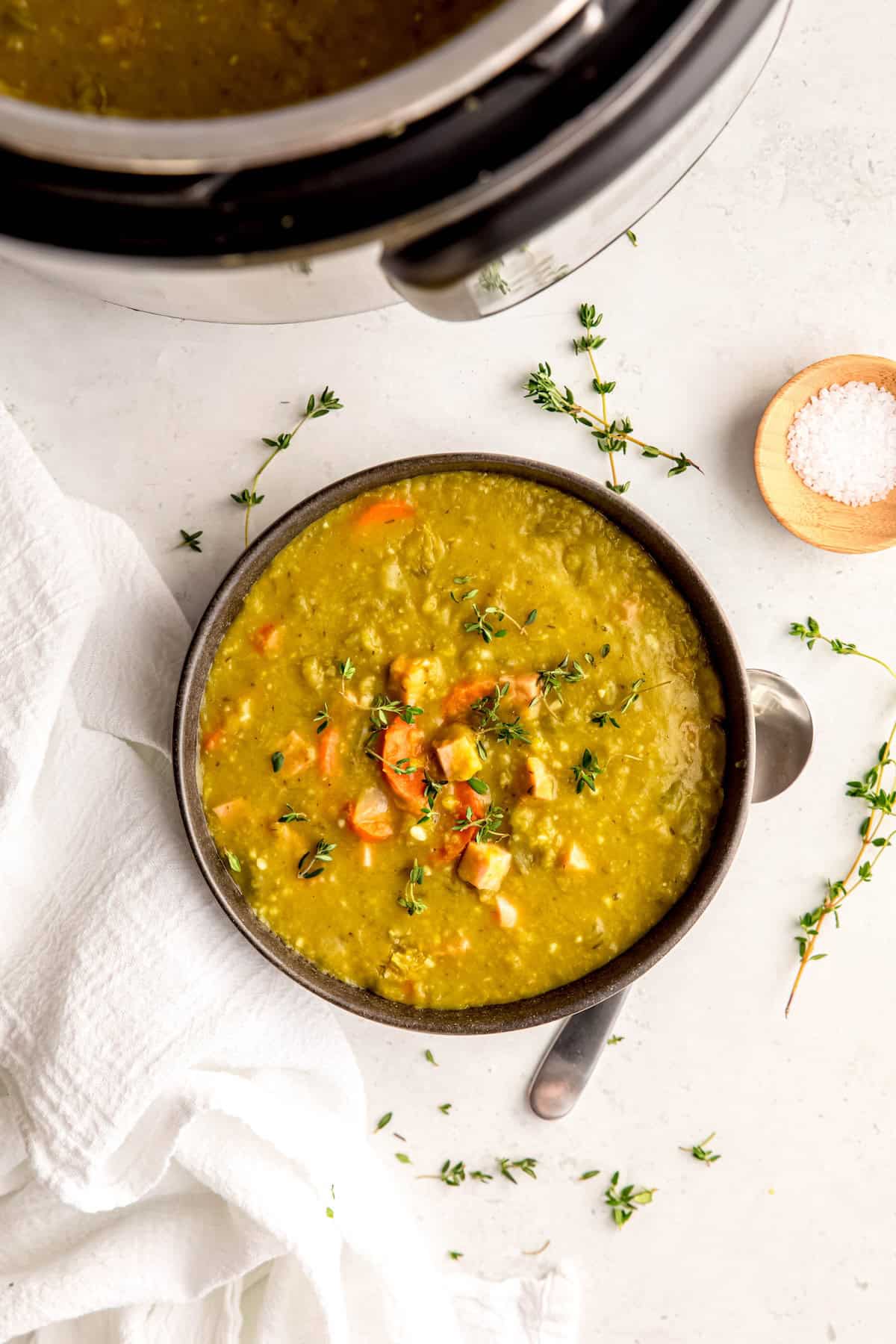 bowl of split pea ham hock soup on a white table with the instant pot framing the top of the shot.