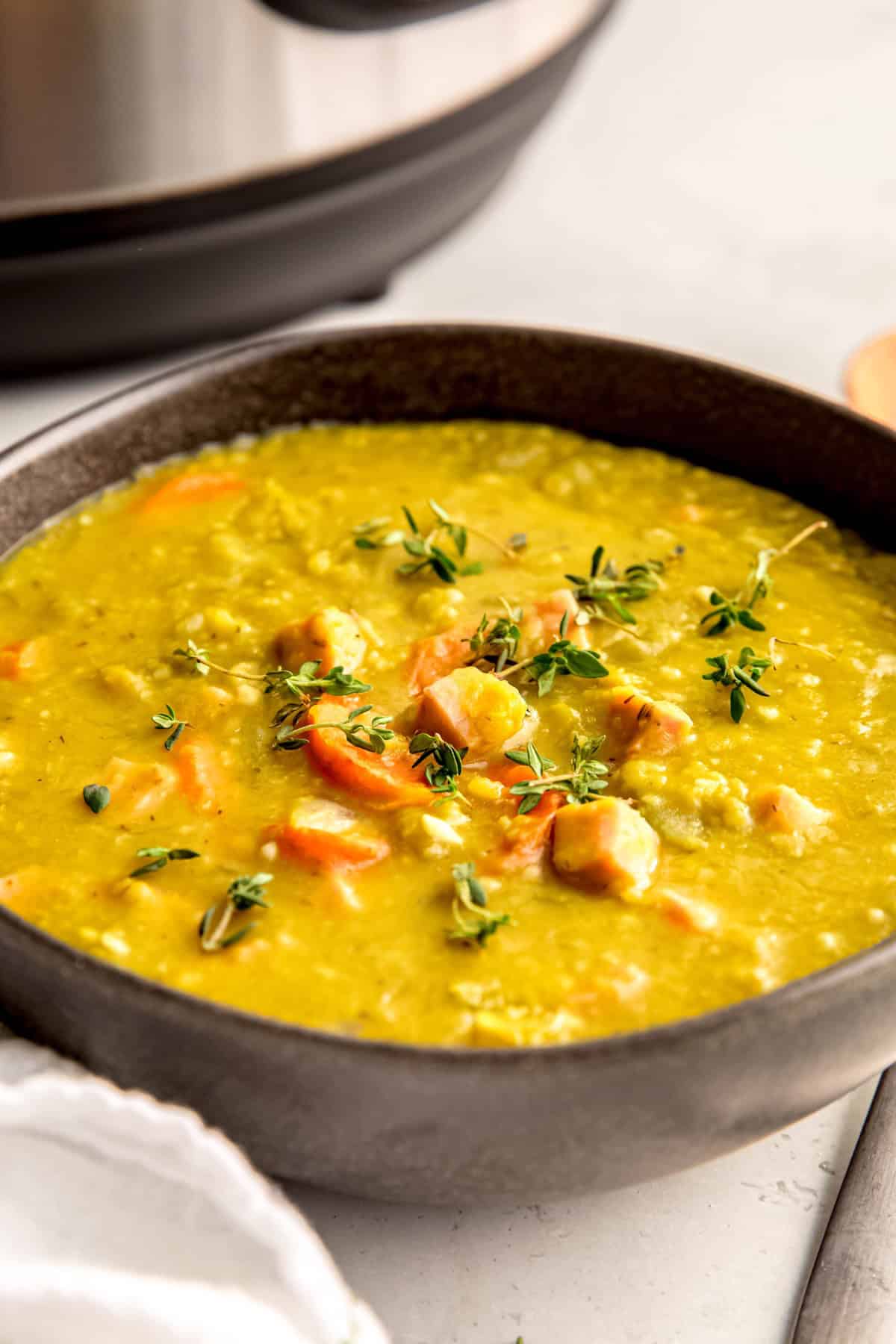 45 degree angle shot of a black bowl filled with instant pot split pea ham hock soup on a white table with the instant pot blurred out in the background.