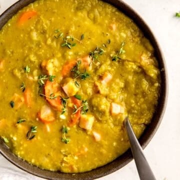 black bowl of instant pot split pea soup with ham garnished with fresh thyme leaves.